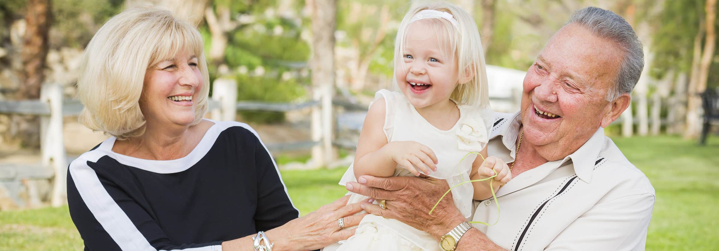 Grandparents walking outside while holding their grand daughter up in the air and laughing