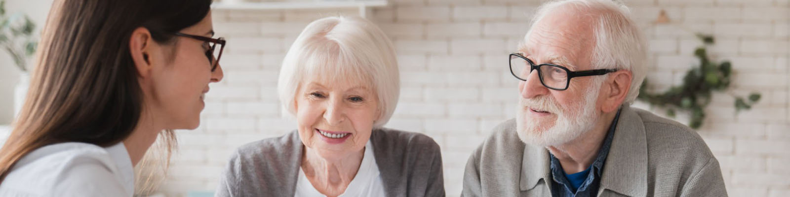 A senior man and woman sitting together at a table across from an insurance specialist while smiling