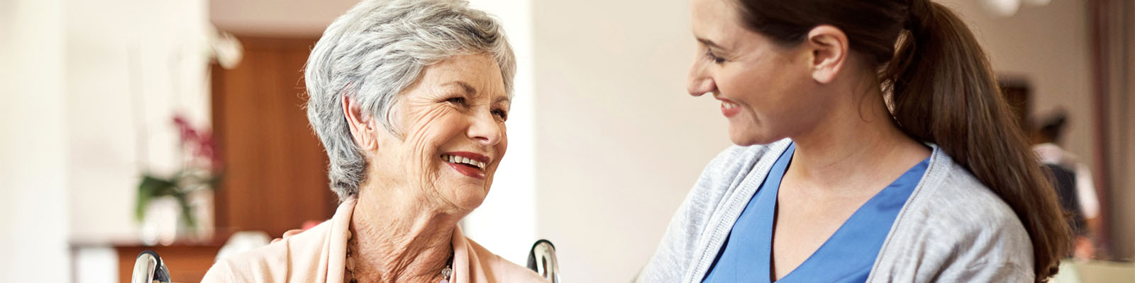 A senior living woman looking up at her female nursing assistant while she sits in a wheelchair