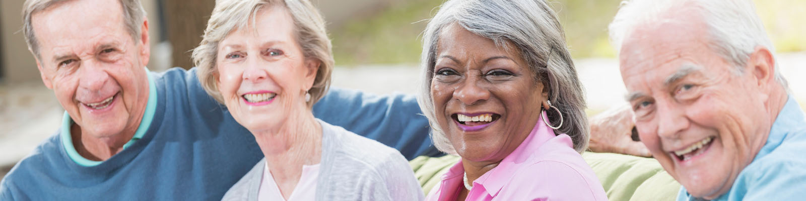 Four senior living residents sitting outdoors on a couch smiling