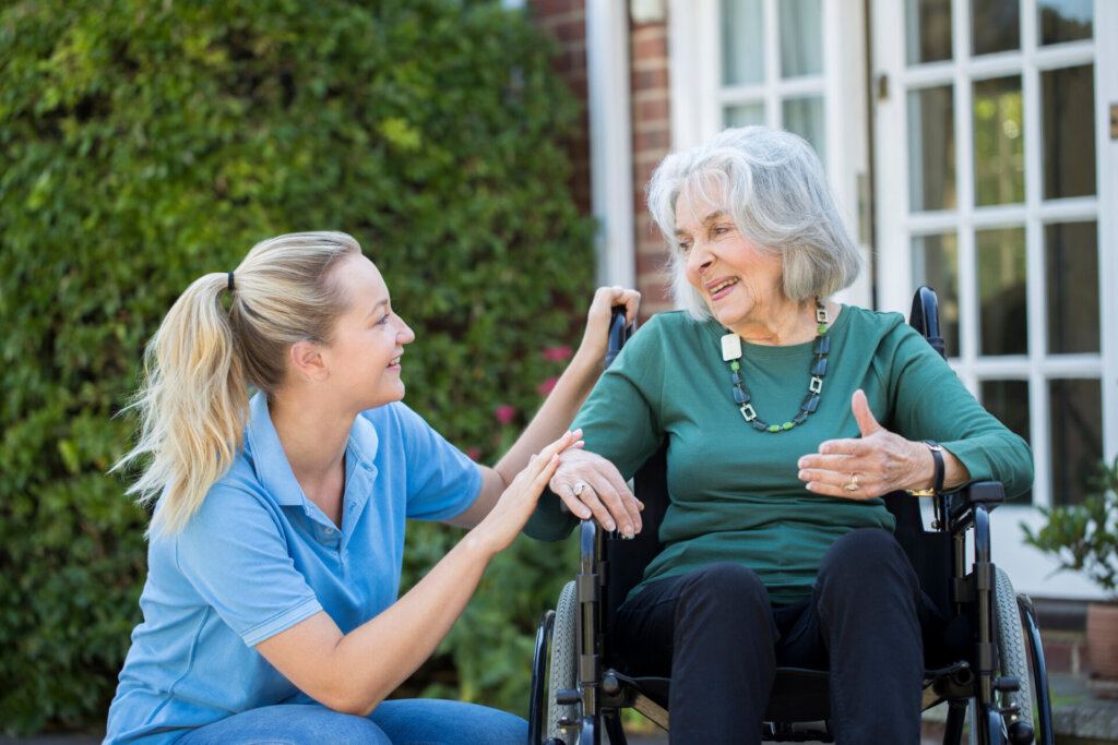 A senior woman sitting in a wheelchair looking over at her nursing assistant